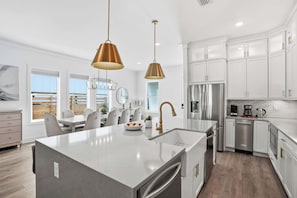 A modern kitchen with white cabinetry, stainless steel appliances, and a central island with a sink and a vase of flowers.