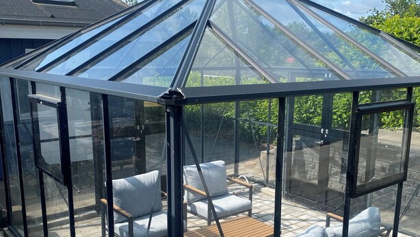 A greenhouse with a glass roof, a wooden table, and cushioned seating. - 2-family activity cottage (Rønde)