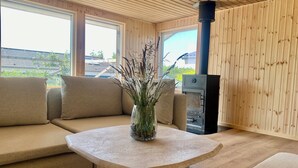 A room with a wooden interior, a sofa, a table with a vase, and a wood-burning stove. - 2-family activity cottage (Rønde)