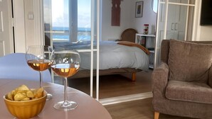 Una stanza con un letto, un divano, un tavolo da pranzo con una ciotola di patatine e bicchieri da vino, e una vista attraverso una porta vetrata.