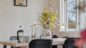 A dining table with chairs, a coffee maker, a pitcher, and a vase with flowers.