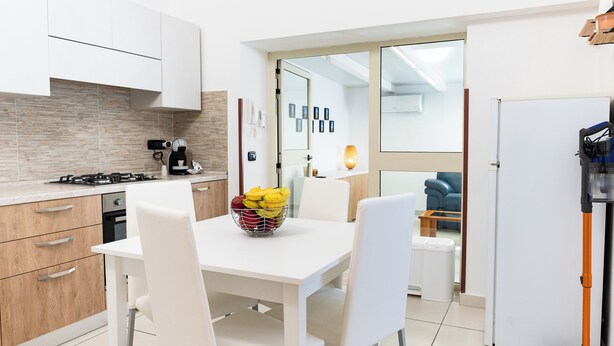 A modern kitchen with white cabinets, a gas stove, and a dining area with a white table and chairs.