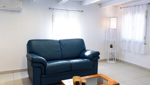 A modern living room with a blue leather sofa, a glass-top coffee table, and a white air conditioning unit on the wall.