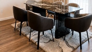 En matplats med ett bord i marmor, fyra stolar, en kristallkrona, en stor abstrakt målning och ett fönster med gardiner.