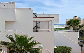 A modern building with a staircase leading to a balcony, overlooking a beach and palm trees. - Beach front apartment in Palomares (Cuevas de Almanzora)