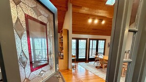 Un pasillo con piso de madera que conduce a un comedor con techo alto y ventanas amplias.