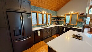 Una cocina moderna con armarios oscuros, un refrigerador de acero inoxidable, una encimera blanca y un techo de madera.