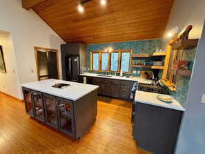 A modern kitchen with a central island, dark cabinets, and a wooden ceiling.