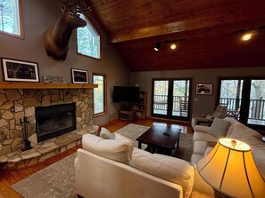A cozy living room with a stone fireplace, a mounted deer head, a television, and a comfortable seating area with a lamp.