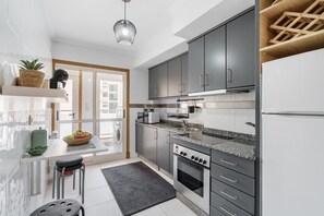 A modern kitchen with grey cabinets, a built-in oven, and a microwave. There is a window providing natural light and a view of the outside. - Sunny Beachside Escape by Minho s Guest (Povoa De Varzim)