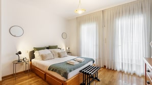 A neatly arranged bedroom with a wooden bed, bedside tables, a bench, and a hanging light fixture. - Sunny Beachside Escape by Minho s Guest (Povoa De Varzim)