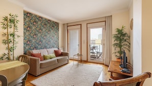 A living room with a sofa, a dining table, and a TV. There are plants and a patterned wall. - Sunny Beachside Escape by Minho s Guest (Povoa De Varzim)