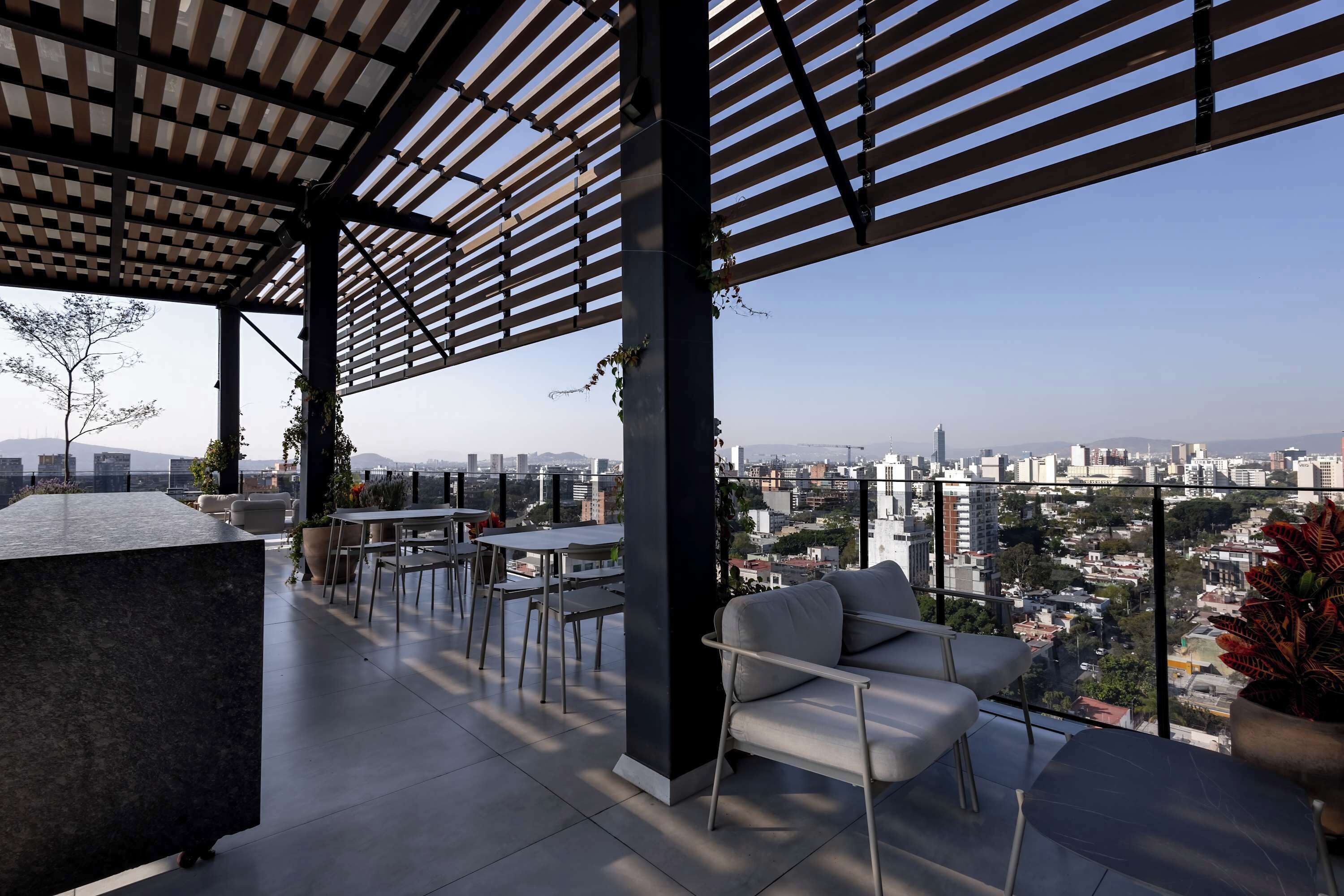 Terraza en la azotea con vistas a un paisaje urbano, que cuenta con una pérgola, zona de estar y plantas en macetas.