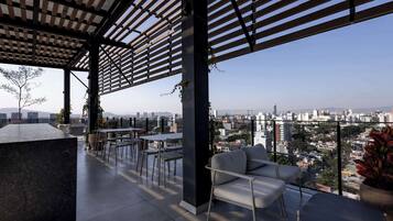 Terraza en la azotea con vistas a un paisaje urbano, que cuenta con una pérgola, zona de estar y plantas en macetas.