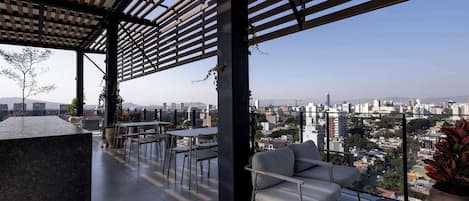 Terraza en la azotea con vistas a un paisaje urbano, que cuenta con una pérgola, zona de estar y plantas en macetas.