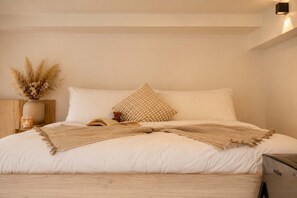A neatly made bed with a beige throw blanket, a small bedside table with a candle, and a vase with dried flowers. - Trendy Loft | Walk to Guadalajara's Best Spots (Guadalajara)