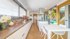 Een moderne keuken met een lange aanrecht, witte kasten en een eethoek met een witte tafel en stoelen.