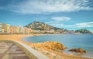 A coastal cityscape with a sandy beach, a rocky outcrop, and a hill with buildings. - Luxurious home in BLANES (BLANES)
