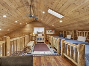 Interior de una cabaña de troncos con un dormitorio en el altillo, una cama individual, un escritorio y una silla.