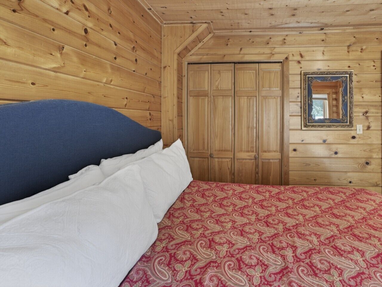 Habitación con paneles de madera, una cama, un armario y un espejo.