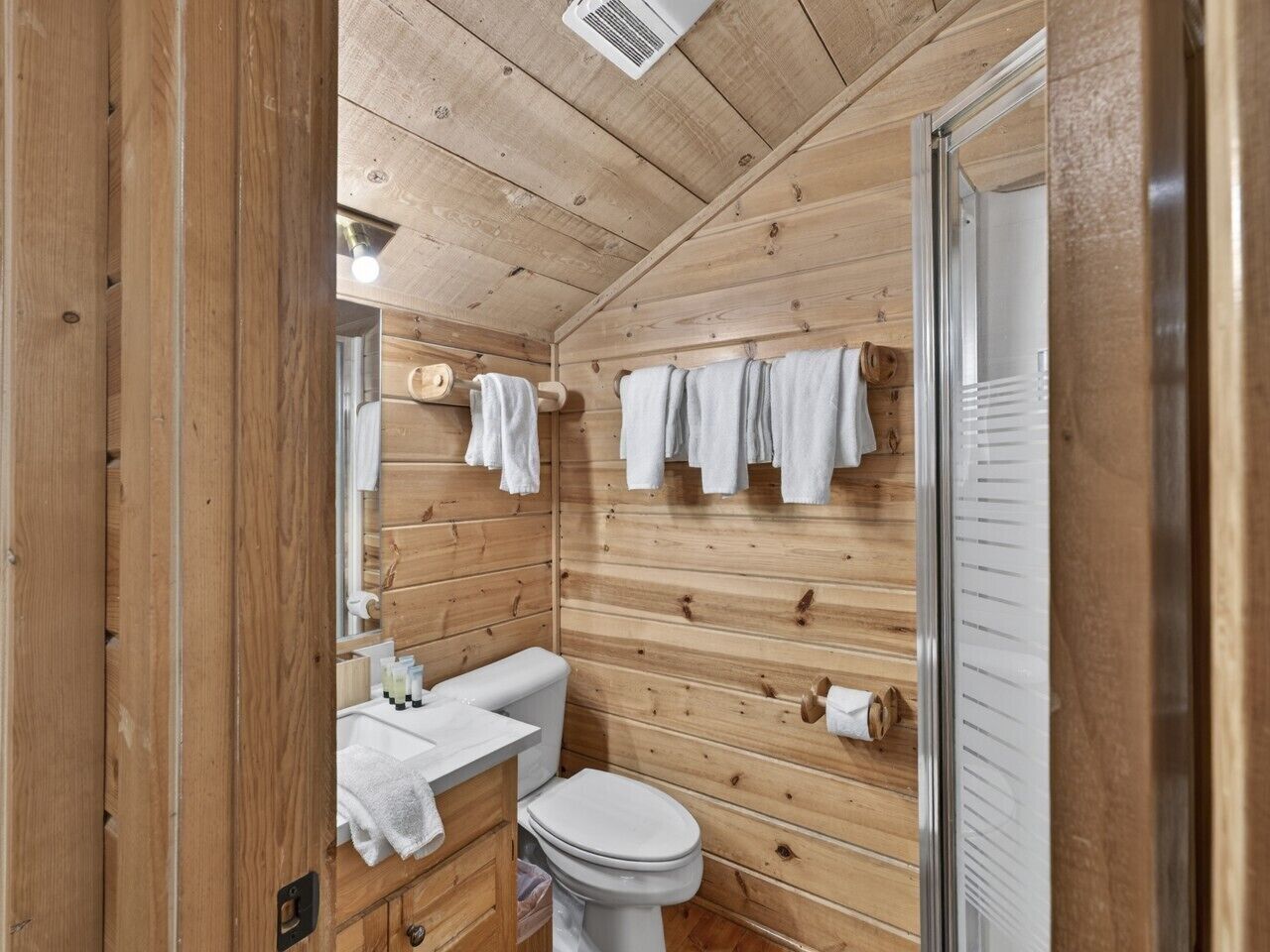 A wooden cabin bathroom with a toilet, sink, and towel rack.