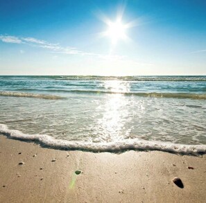 Una playa con agua cristalina, reflejos de sol en la superficie y un mar tranquilo.