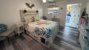A bedroom with a wooden headboard, a bed with a leaf-patterned bedspread, a ceiling fan, and a window with a view of the outside. - Beach Paradise on Venice Island (Venice)