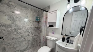 A bathroom with a marble wall, a shower curtain, a toilet, a sink, and a mirror. - Beach Paradise on Venice Island (Venice)