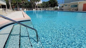 A clear blue pool with a metal ladder, surrounded by palm trees and a building with a balcony. - Beach Paradise on Venice Island (Venice)