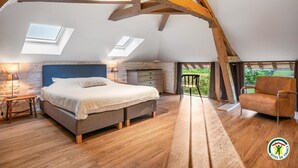 A bedroom with a bed, a stone wall, a wooden ceiling, and a view of the outdoors. - Gîtes de France® - Le Gîte du Château (BERTREVILLE SAINT OUEN)