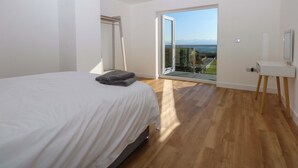 Ein Schlafzimmer mit einem großen Bett, einer Glasschiebetür, die auf einen Balkon führt, und einem kleinen Schreibtisch mit Stuhl.