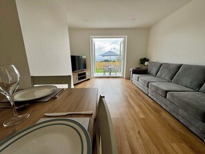 Ein Wohnzimmer mit einer Couch, einem Fernseher auf einem Lowboard, einem Esstisch mit Besteck und einem Weinglas.