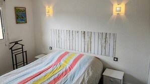 A bedroom with a bed, bedside tables, a wall-mounted light fixture, and a painting on the wall. - AMARINE Residence – 2-Bedroom Apartment, Terrace, Heated Pool  et  WiFi (CAPBRETON)
