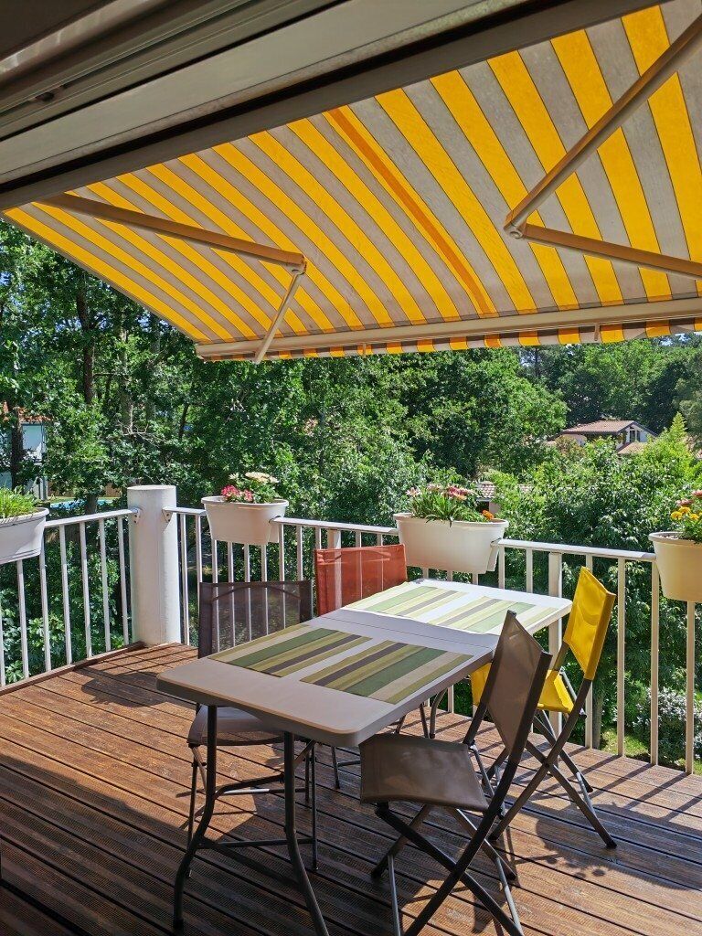 Um deck de madeira com mesa, cadeiras, um toldo listrado e plantas em vasos.