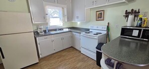 A compact kitchen with white cabinets, a stove, a microwave, and a sink.