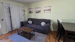 Ein Wohnzimmer mit grauem Sofa, einem Holztisch, einem Kleiderständer und einem Esstisch mit Stühlen.