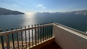 Un balcon offrant une vue sur une mer calme, un paysage urbain lointain et un ciel dégagé.