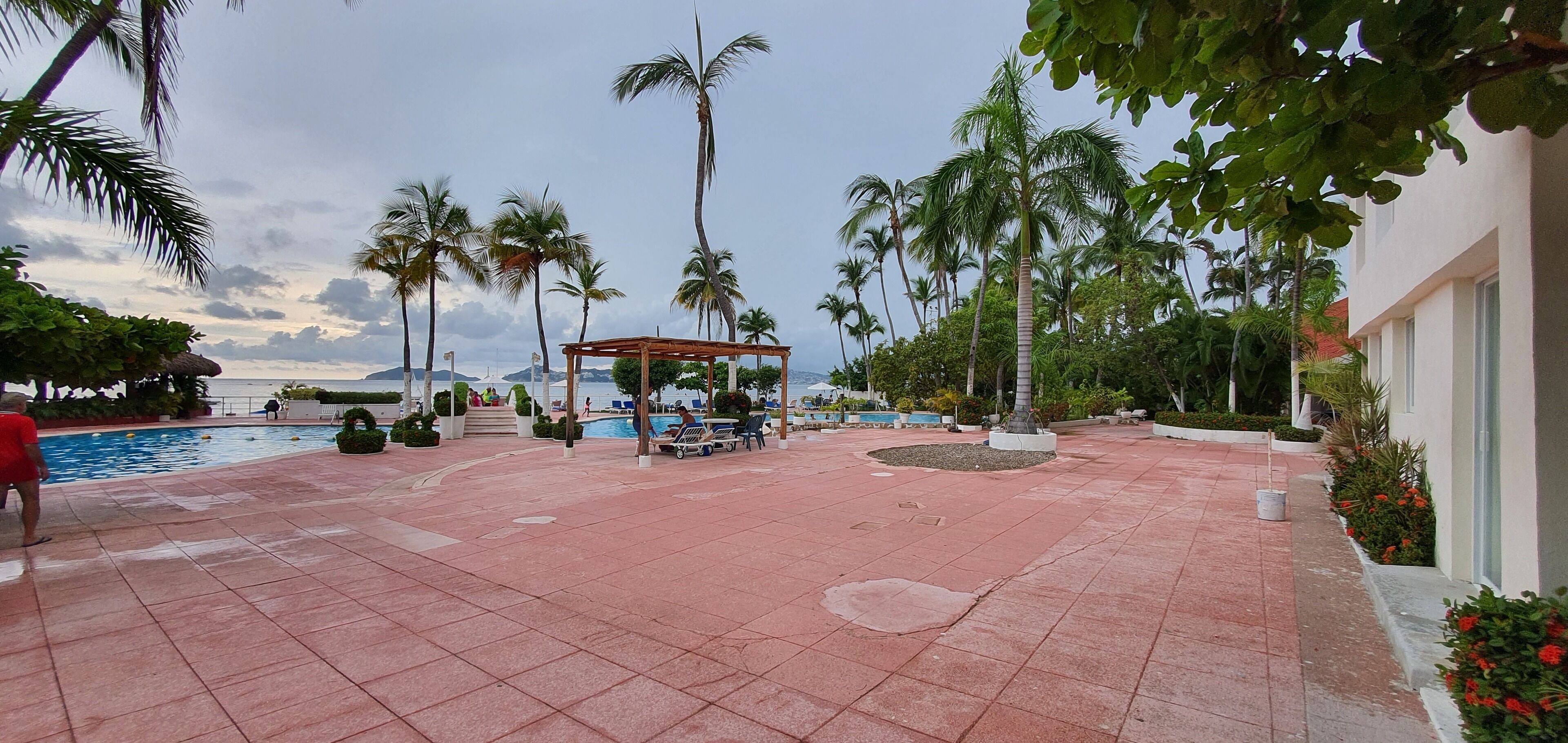 A pool area with tiled flooring, palm trees, and a gazebo.