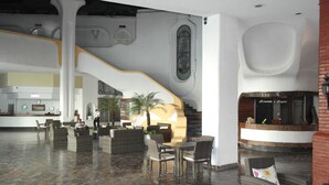 Un hall d’entrée spacieux avec un escalier central, des meubles en osier et un comptoir d’accueil.
