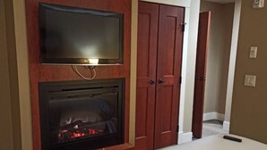 A hotel room with a bed, a flat-screen TV mounted on a wooden wall, and a fireplace. - Stunning 2-BR Suite with Hot Tub & Mountain Views (Canmore)
