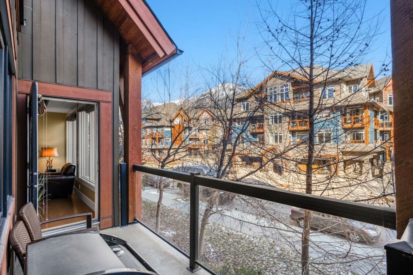 A balcony with a view of multi-story buildings, a chair, and a table with a lamp.