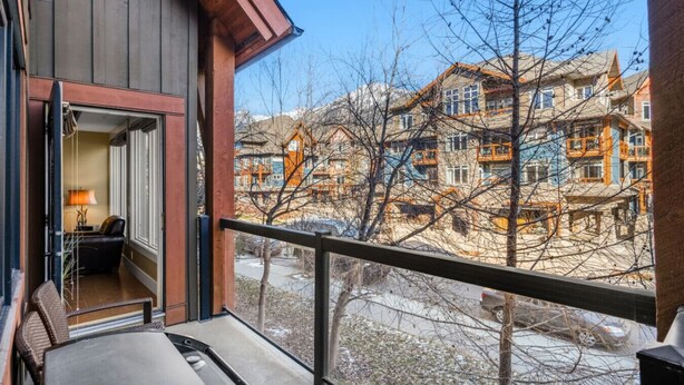 A balcony with a view of multi-story buildings, a chair, and a table with a lamp. - Elegant Mountain Retreat | Pool and Hot Tub (Canmore)