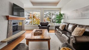 Een moderne woonkamer met een open haard, een leren bank en een groot raam met uitzicht op met sneeuw bedekte bomen.