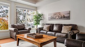 Een woonkamer met twee leren banken, een houten salontafel en een groot raam met uitzicht op besneeuwde bomen.