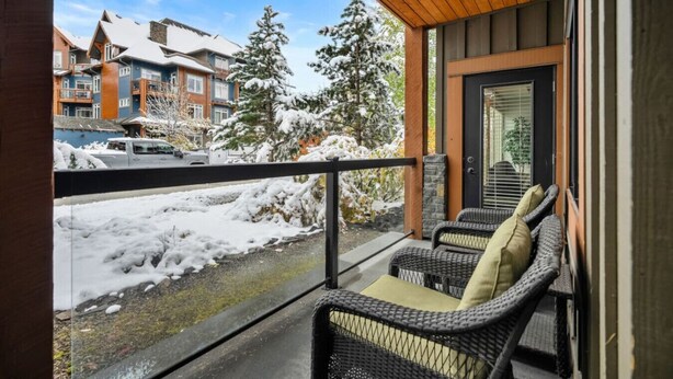 Een balkon met rieten stoelen, een houten plafond en uitzicht op besneeuwde gebouwen en bomen.