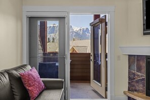 Ein Zimmer mit einer Couch, einem Kamin und einer Glastür zum Blick auf die Berge.