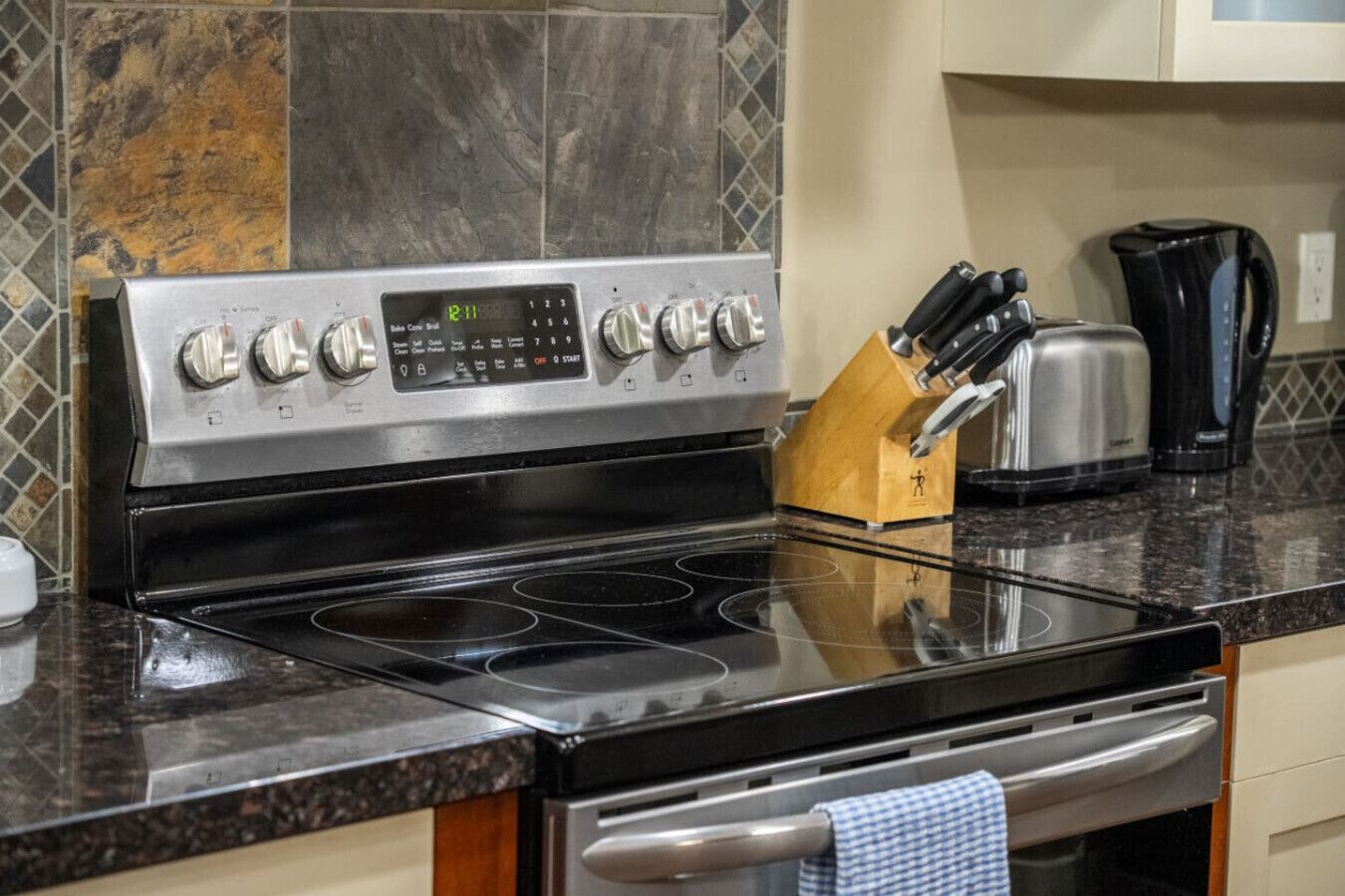Una cucina con un piano cottura in acciaio inossidabile, una sveglia digitale e un portacoltelli sul ripiano.