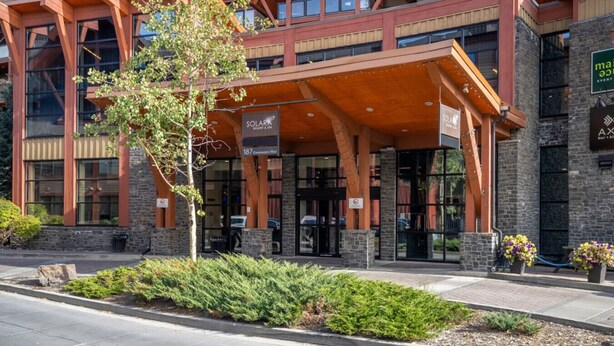 A modern building with a covered entrance, signage for 'SOLARA RESORT & SPA', and a landscaped area with shrubs and a tree. - Modern Condo Retreat 2BR+Sofa Bed | Patio & Trails (Canmore)
