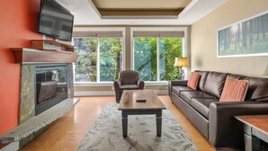 A living room with a fireplace, a sofa, a coffee table, and a television. - Modern Condo Retreat 2BR+Sofa Bed | Patio & Trails (Canmore)