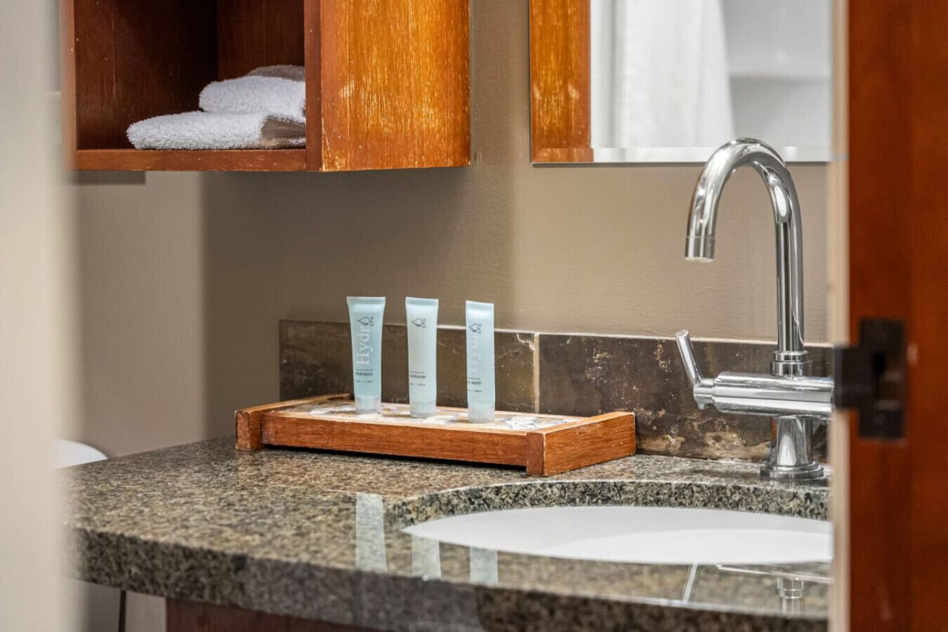 A bathroom with a granite countertop, a wooden shelf with towels, and a mirror above the sink.